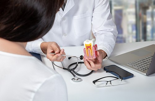 Dentist in white coat explaining root canal to patient at desk