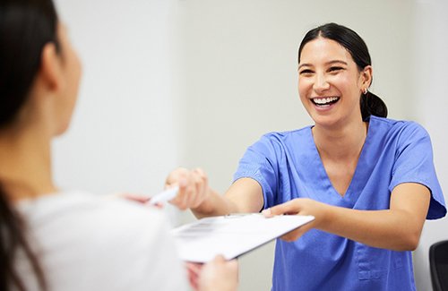 Woman in blue scrubs handing paperwork to patient with pen and clipboard