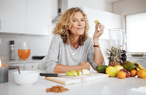 Woman smiling while eating fruit in kitchen