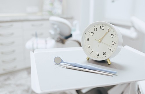 Old-fashioned alarm clock on a white tray with dental instruments in exam room