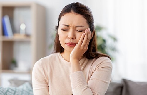 Woman experiencing toothache while sitting on couch at home